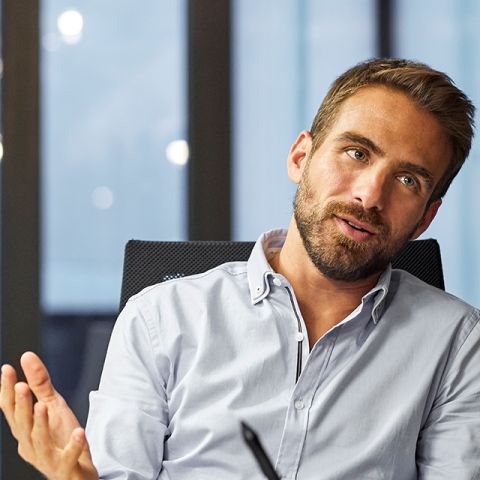 Two individuals engaged in a discussion in a modern office setting, with computers and large windows